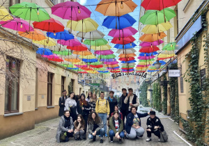 Uczniowie_z_przewodnikiem pod kolorowymi parasolkami w podwórku przy Piotrkowskiej 120