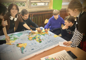Uczniowie pochyleni nad mapą świata w sali geograficznej
