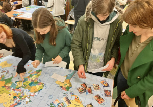 Uczniowie rozwiązują zadania quizu geograficznego na mapie świata