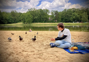 Uczeń siedzi na plaży i karmi kaczki