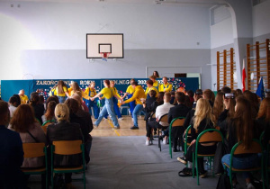 Widok ogólny sali gimnastycznej z uczniami kończącymi klasy czwarte i aktorami na scenie