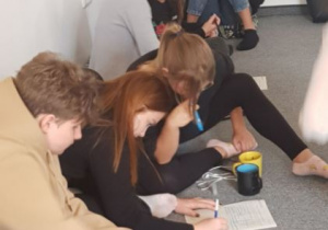 uczniowie siedzą na podłodze i rozwiązują karty pracy